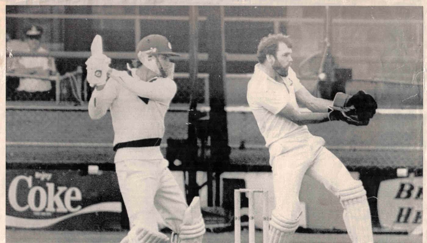 Black and white photograph of two men playing cricket, one wearing an Albion helmet.