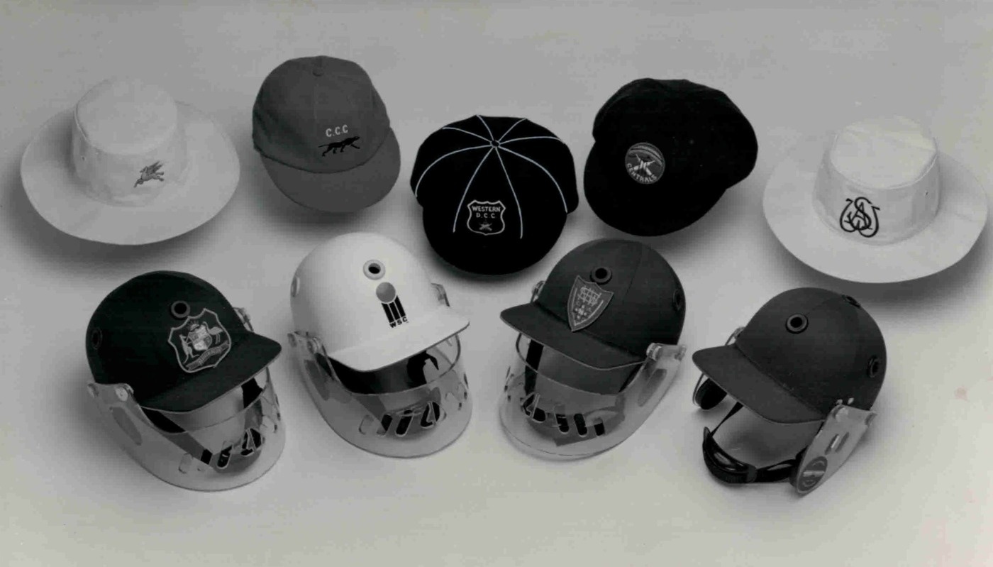 Black and white photograph of four cricket helmets, two sunhats, two Aussie baggy caps and one English fitted baggy.
